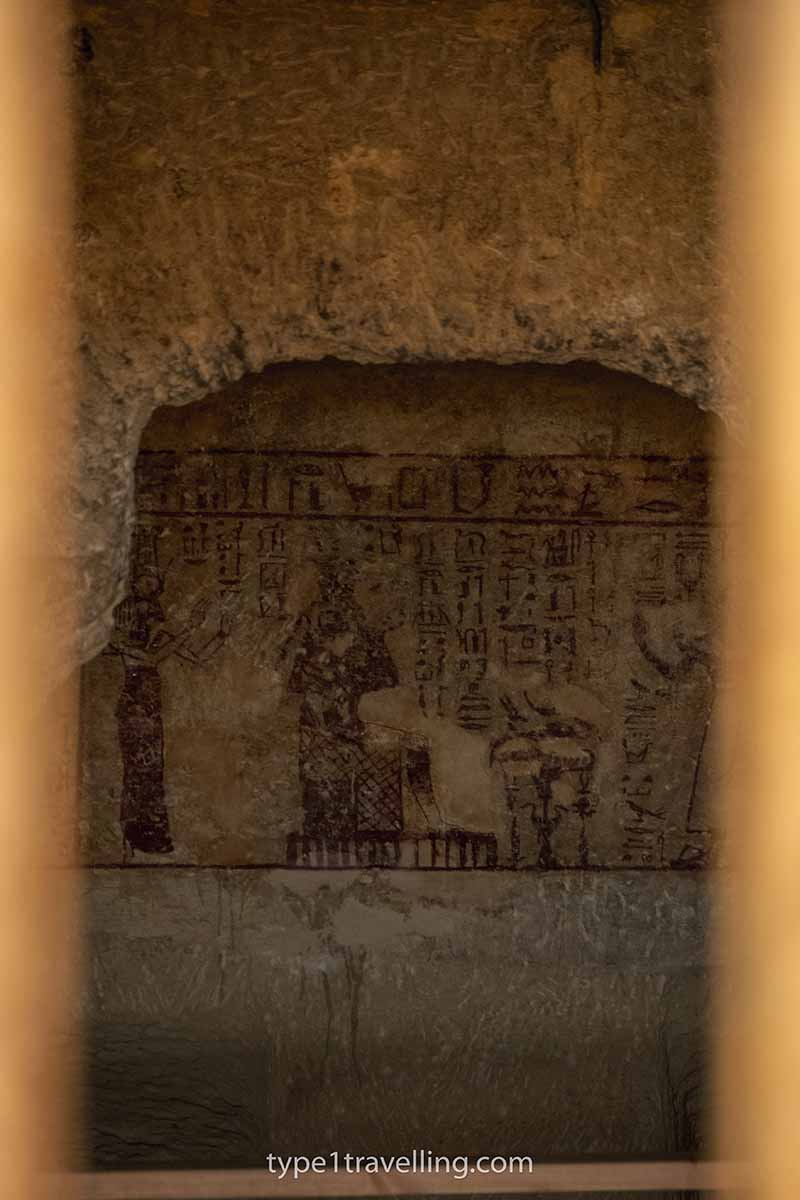 Faded hieroglyphics in an ancient tomb seen through metal bars.