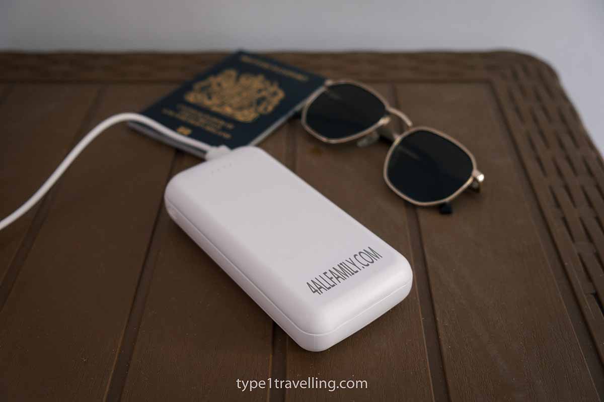 A 4ALLFAMILY Pathfinder power bank and wire, sunglasses and a passport lying on a table.