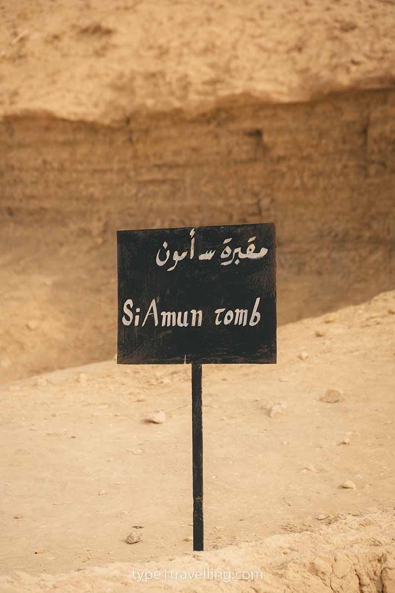 A black sign which reads Si Amun Tomb in English and Arabic.