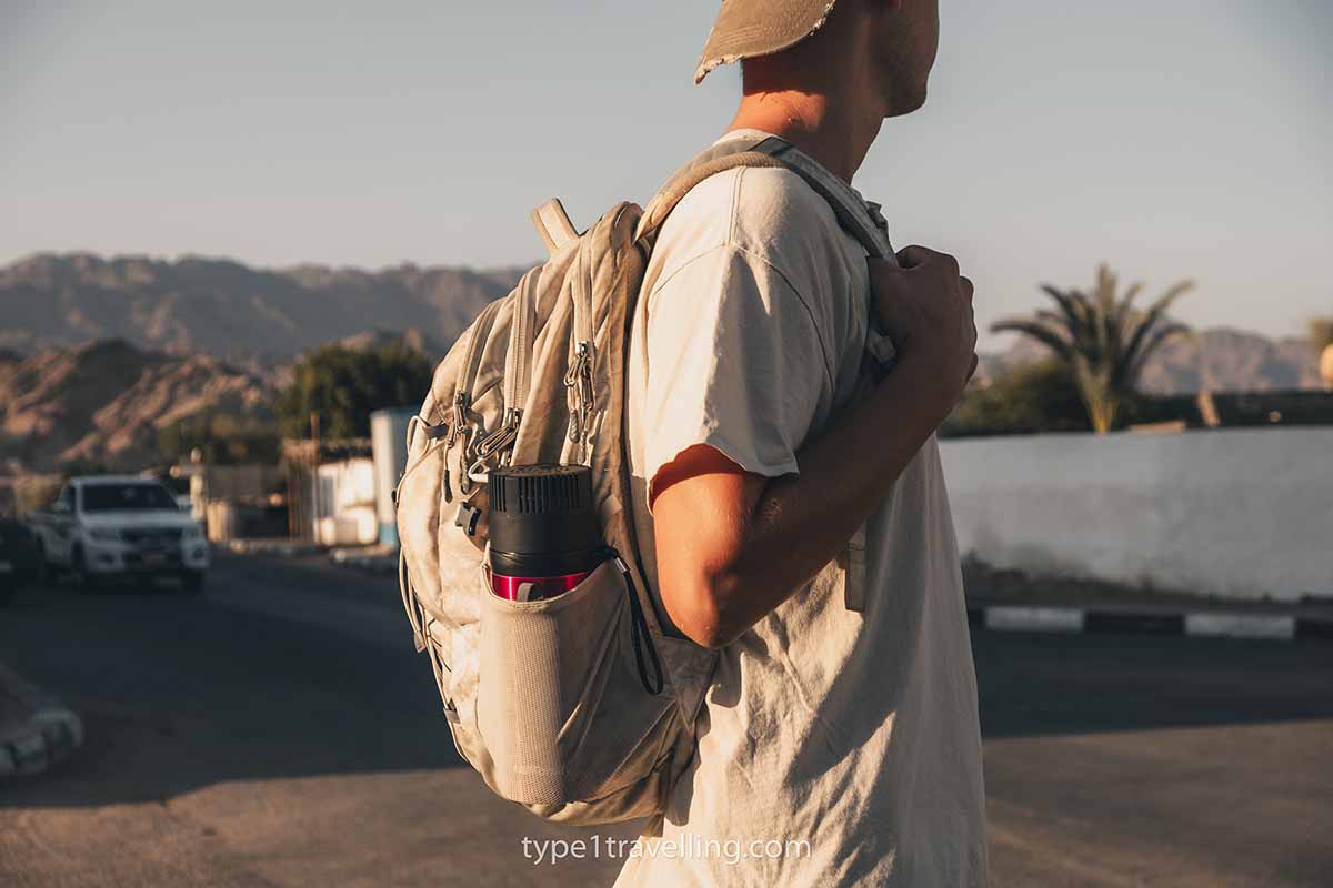 A man standing wearing a backpack which has a 4ALLFAMILY Voyager insulin cooler tucked in the side.