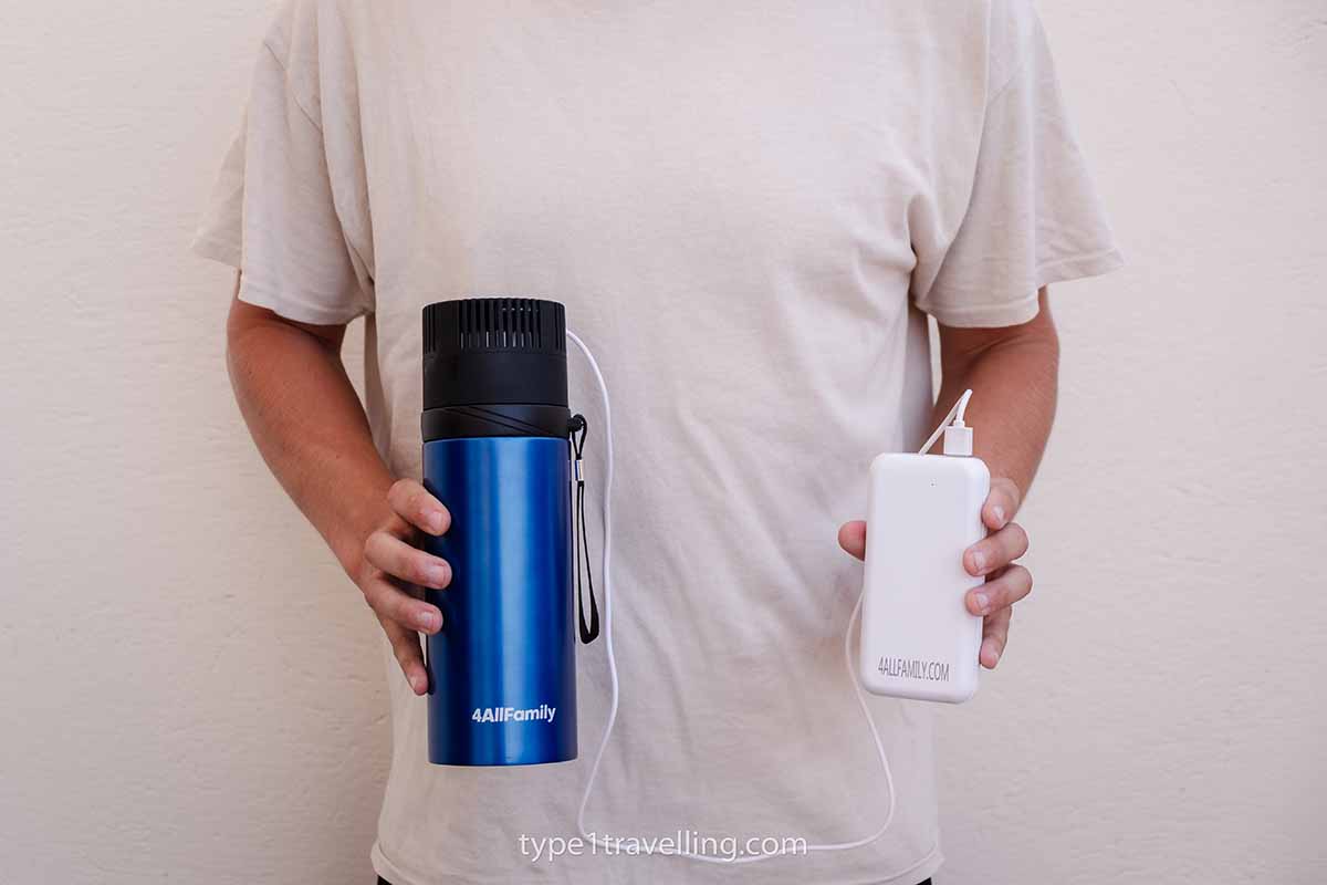 A person holding a blue 4ALLFAMILY Voyager travel fridge and Pathfinder power bank which are connected by a wire.