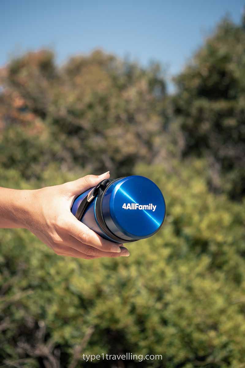 A hand holding a blue 4ALLFAMILY Voyager insulin cooler.