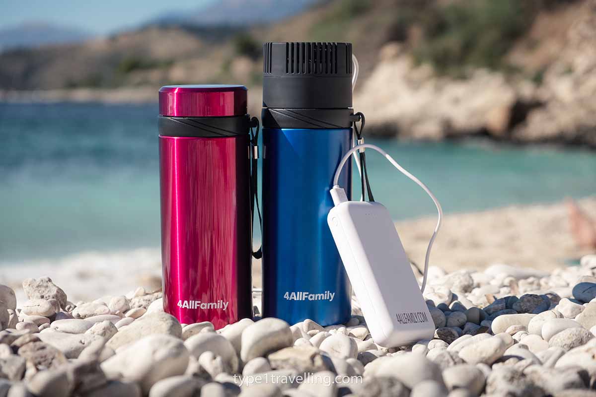 A red and a blue Voyager insulin cooler and a Pathfinder power bank standing next to each other on a pebble beach.