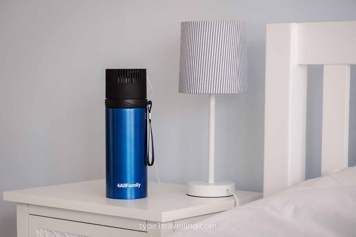 A blue Voyager travel fridge sitting on a bedside table next to a lamp.