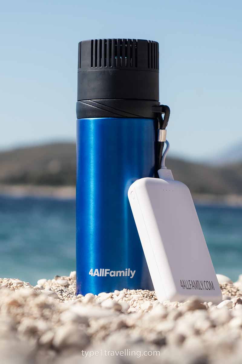 A blue Voyager travel fridge sitting on a pebble beach and plugged into a Pathfinder power bank.