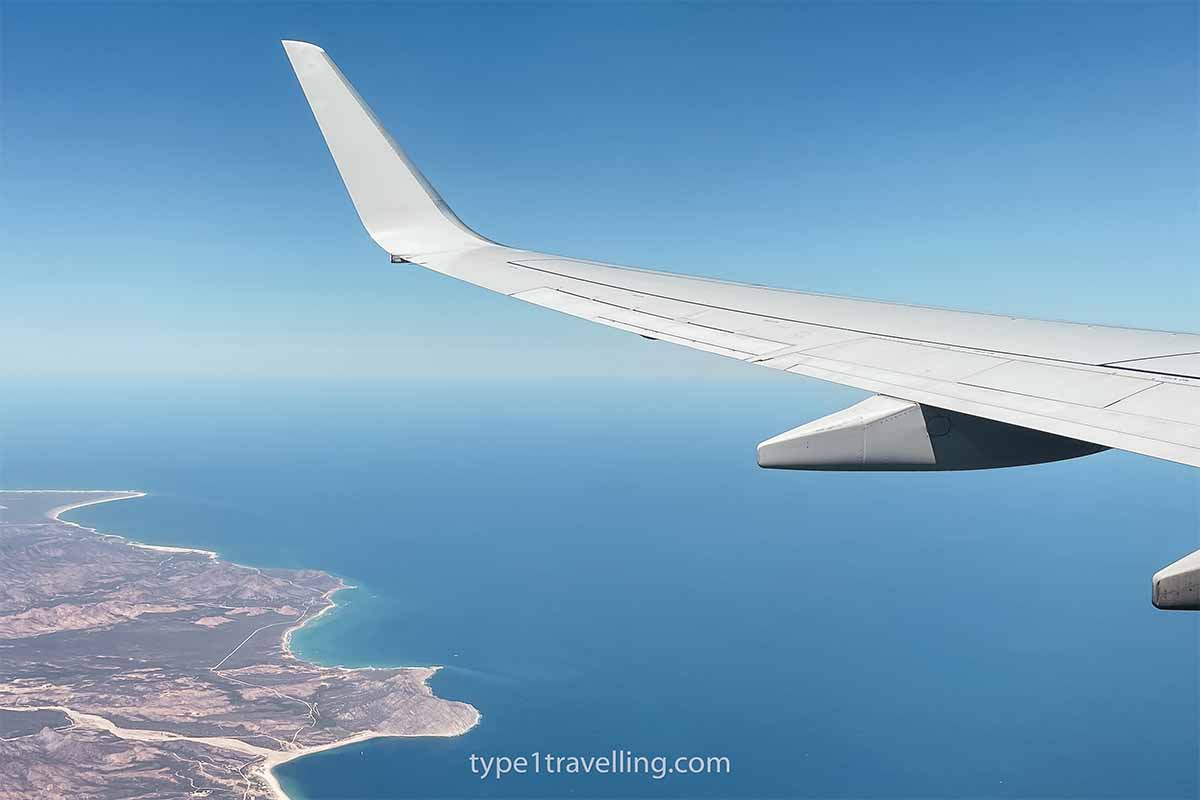 A mid-flight view of an aeroplane wing and coastline.