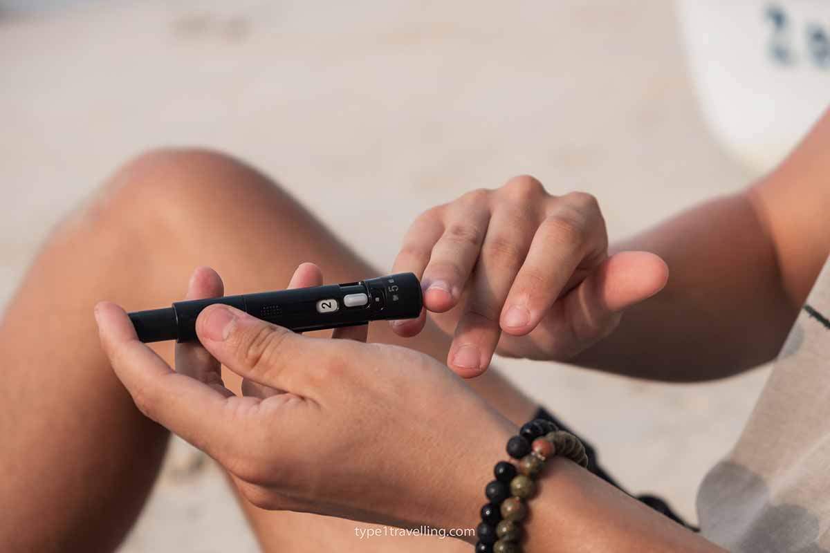 A person pricking their finger to take a blood glucose test while sitting on a beach.