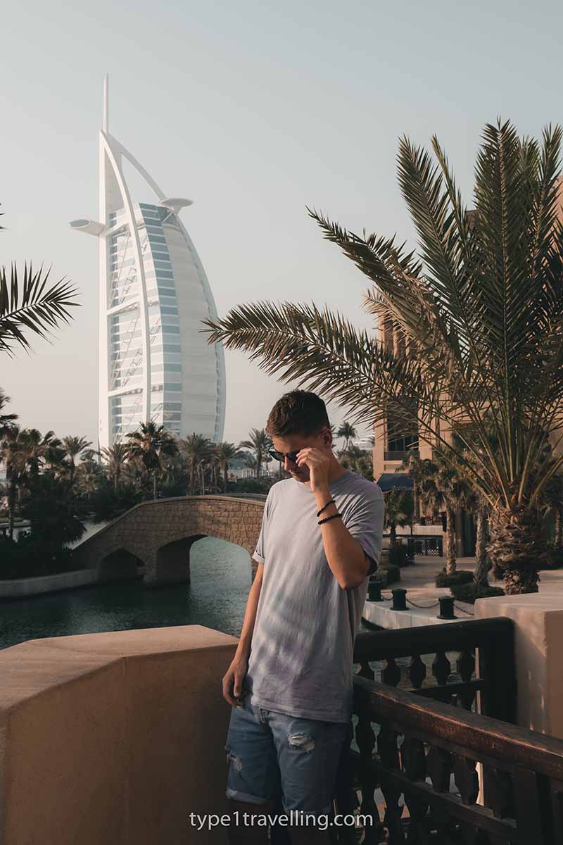 A man glancing down with a hand on his sunglasses with the Burj al Arab in the background.