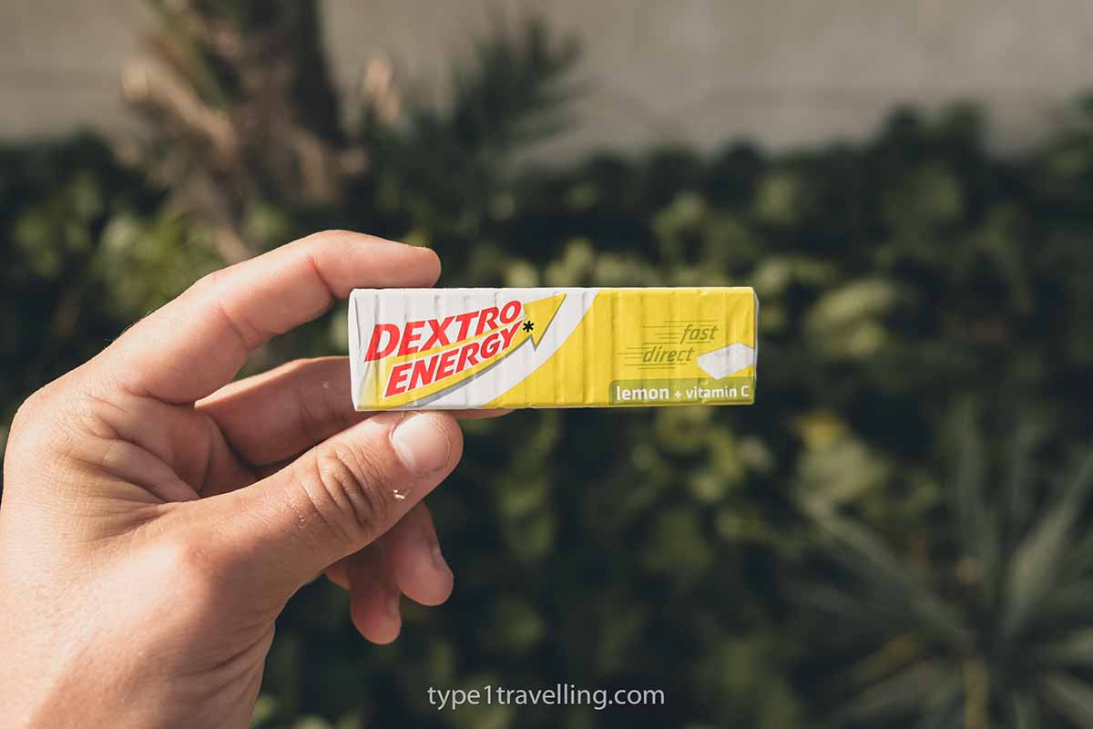 A hand holding a yellow and white packet of lemon flavoured Dextro glucose tablets.