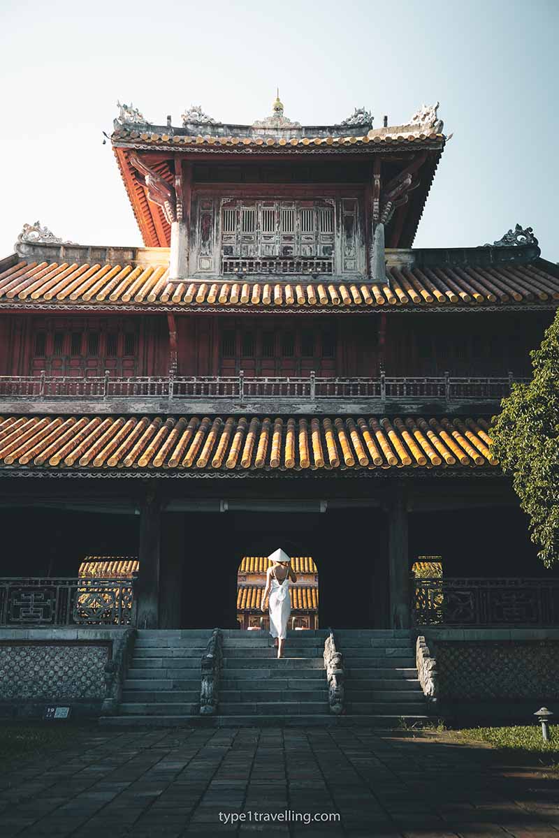 A woman walking up the front steps of an ancient building within the Hue Citadel.