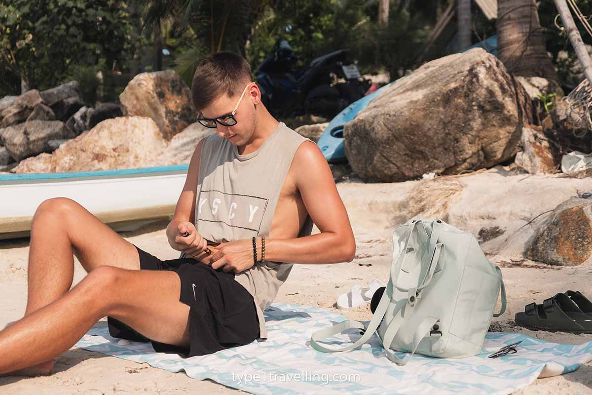 A man injecting insulin while sitting on a beach.