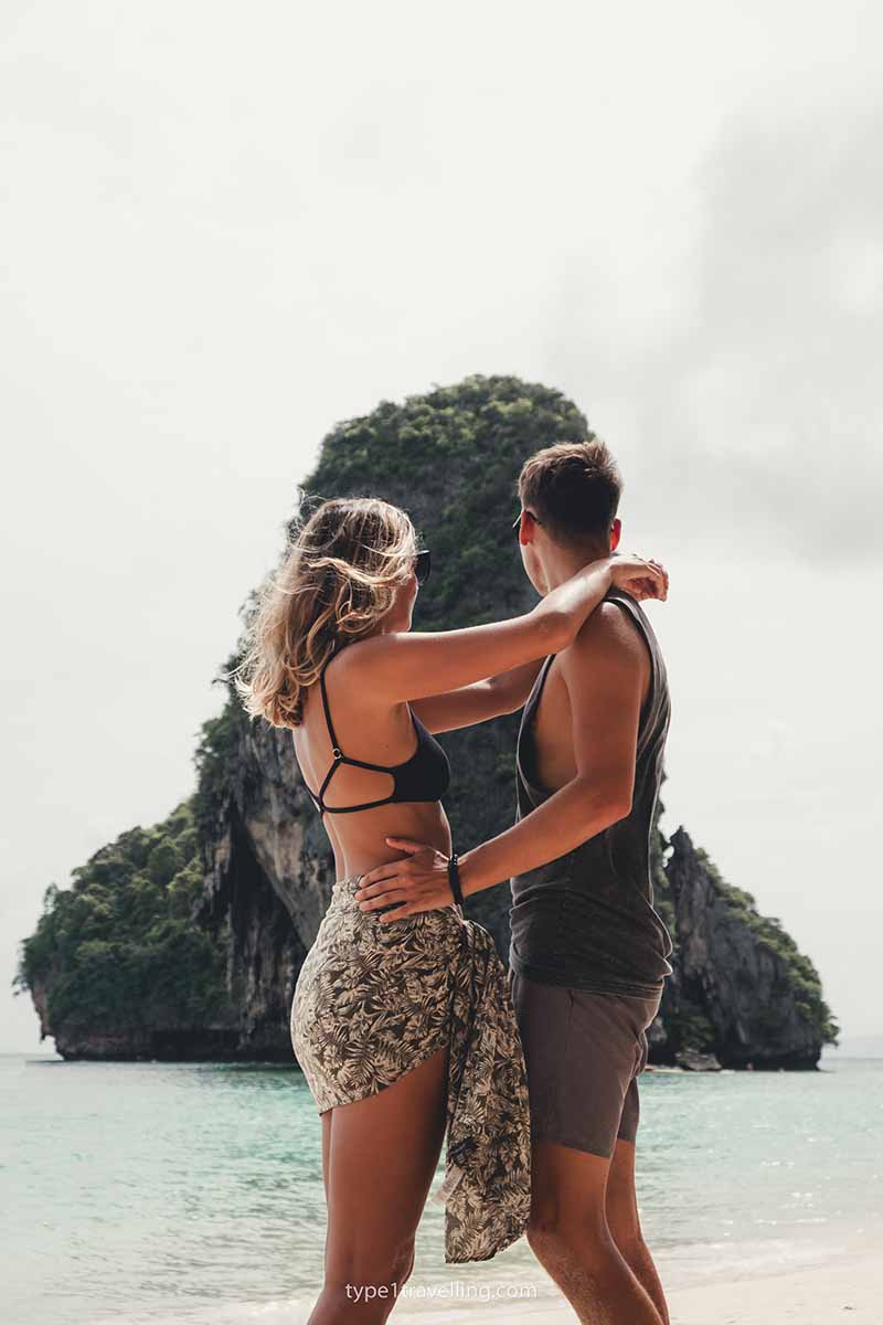 A couple embracing on Phra Nang Cave Beach while looking out at a huge limestone rock formation in the sea.