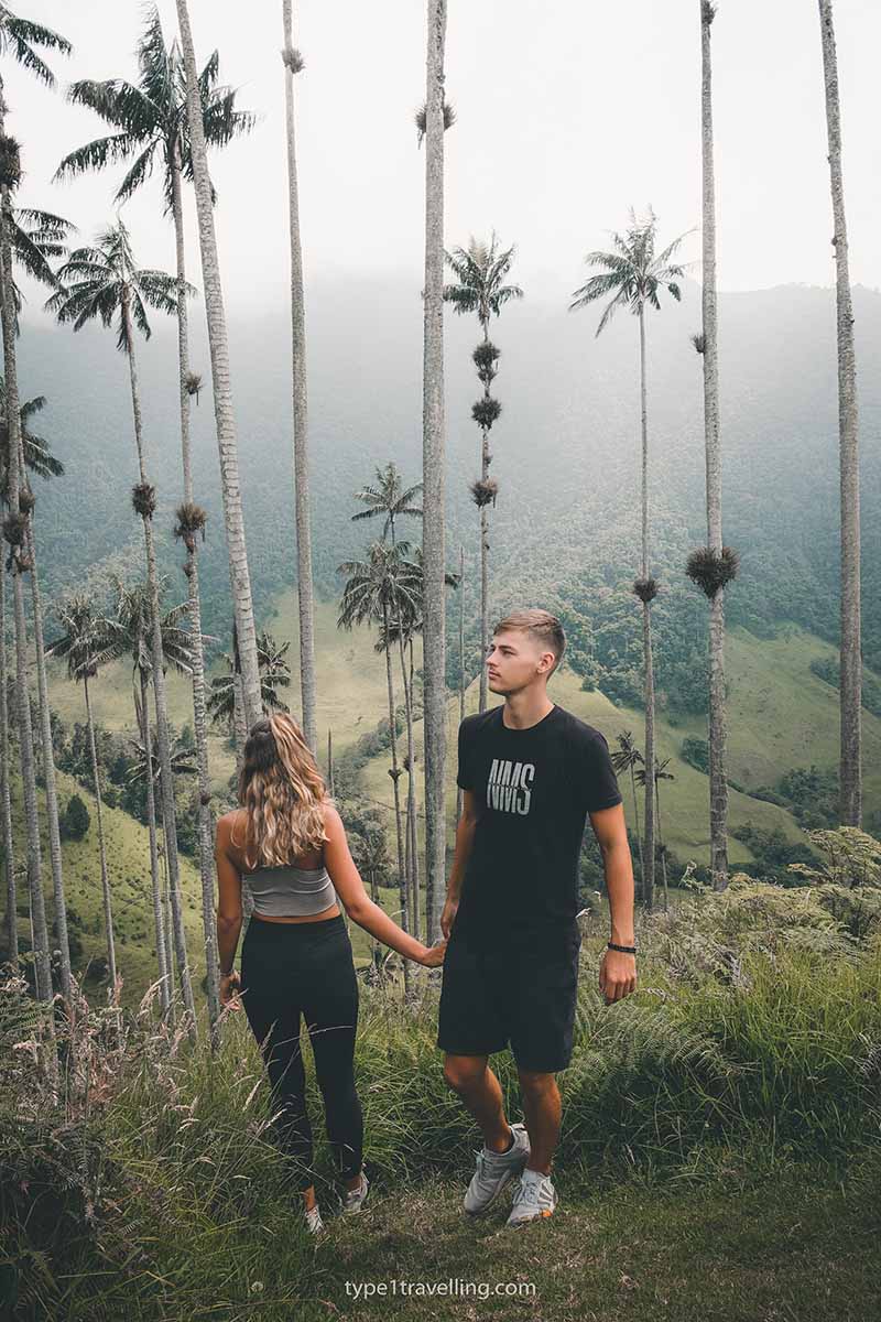 A couple holding hands and surrounded by tall palm trees in Cocora Valley.