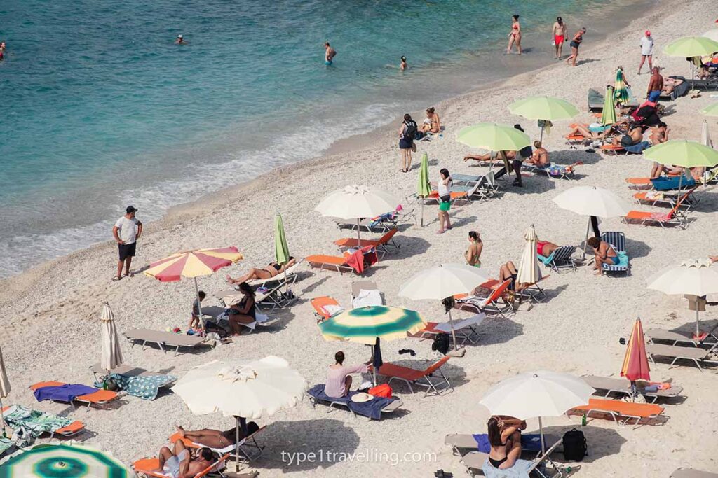 Three rows of people sunbathing on loungers with parasols on the shoreline of Mirror Beach.