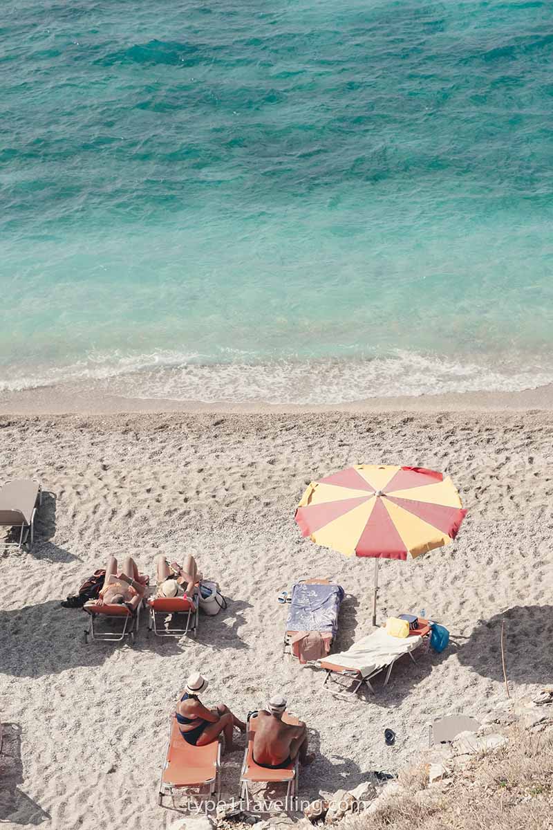 A few people sitting on sun loungers and a yellow and red beach parasol close to the shoreline on Mirror Beach.