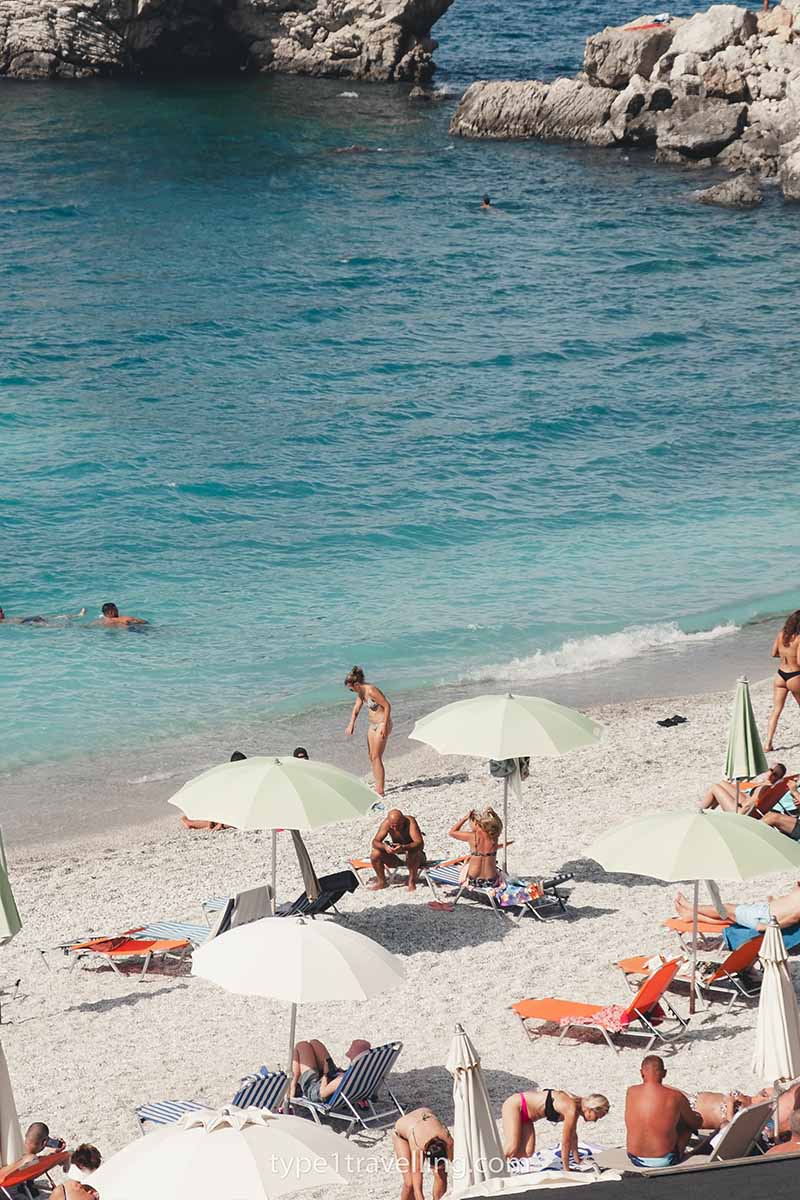 Beach goers lying on sun loungers, sitting on the sand, and swimming in the water of Mirror Beach.