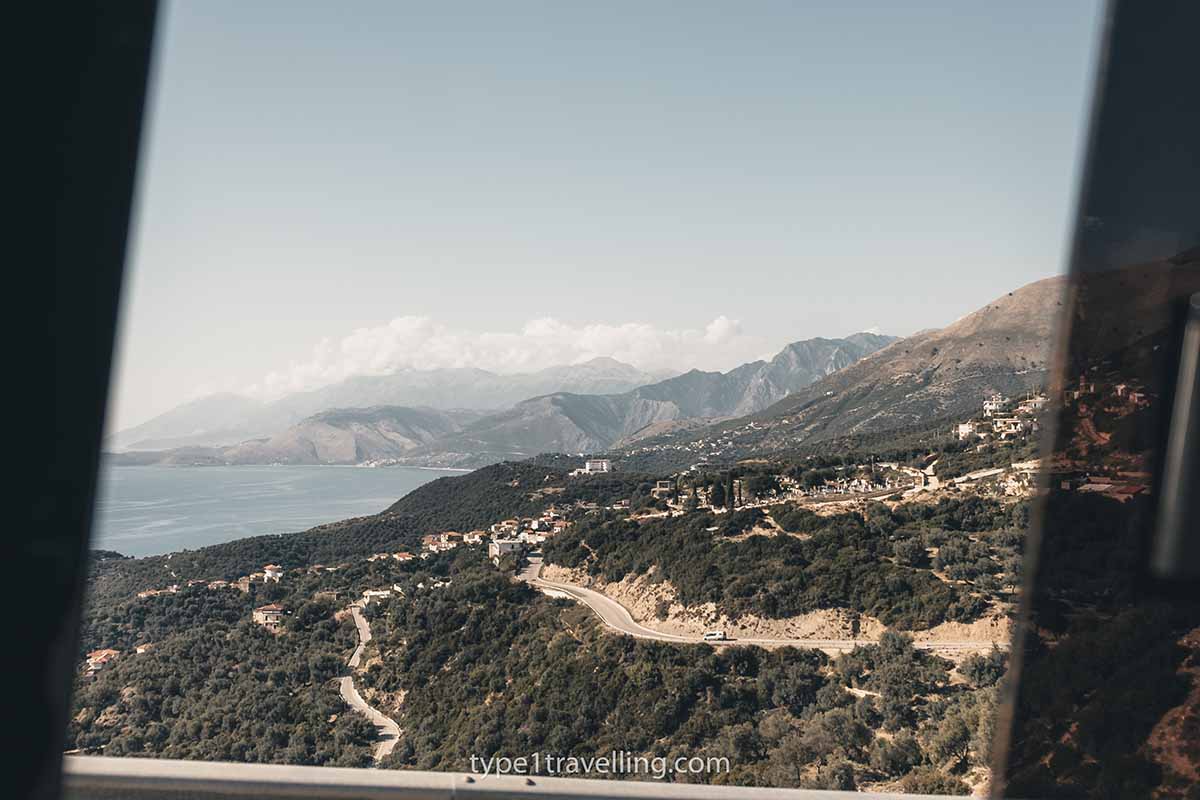 coastal-bus A coastal road, sea, and mountains seen through a vehicle window.