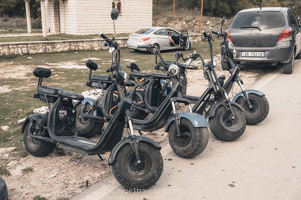 Four electric scooters parked in a row at the side of a road.