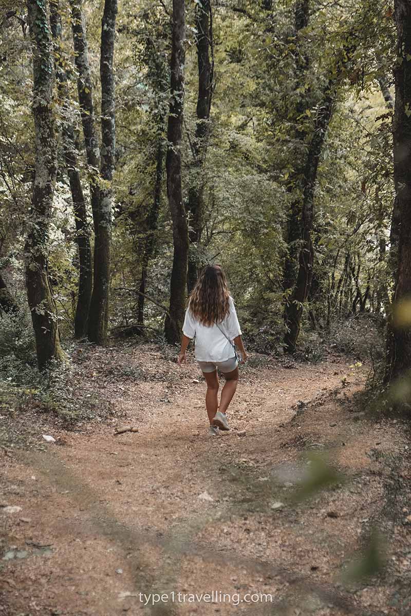 A woman walking along a dirt forest trail surrounded by trees.
