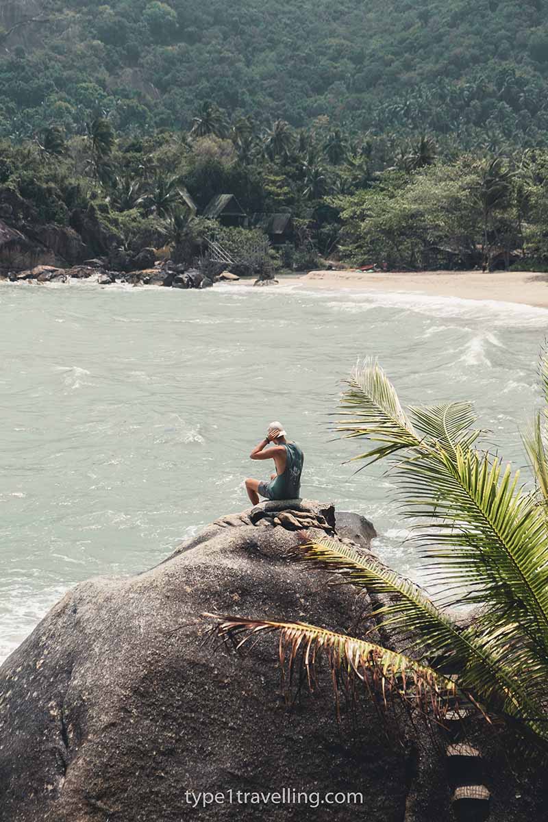 A person sitting on a large boulder overlooking the bay of Haad Sadet.