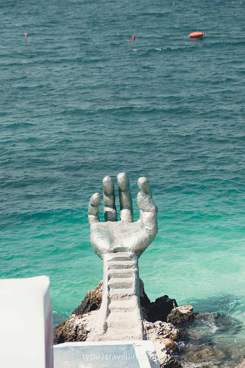 A giant silver statue of a hand above turquoise water.