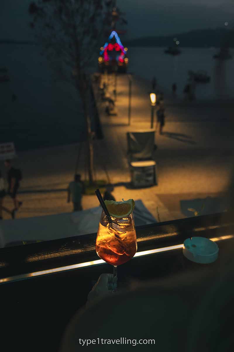 A person overlooking the Saranda Promenade at night with an Aperol Spritz at Jericho Cocktail Bar.