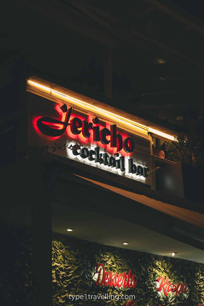 The sign for Jericho Cocktail Bar lit up at night with orange, red, and white lights.