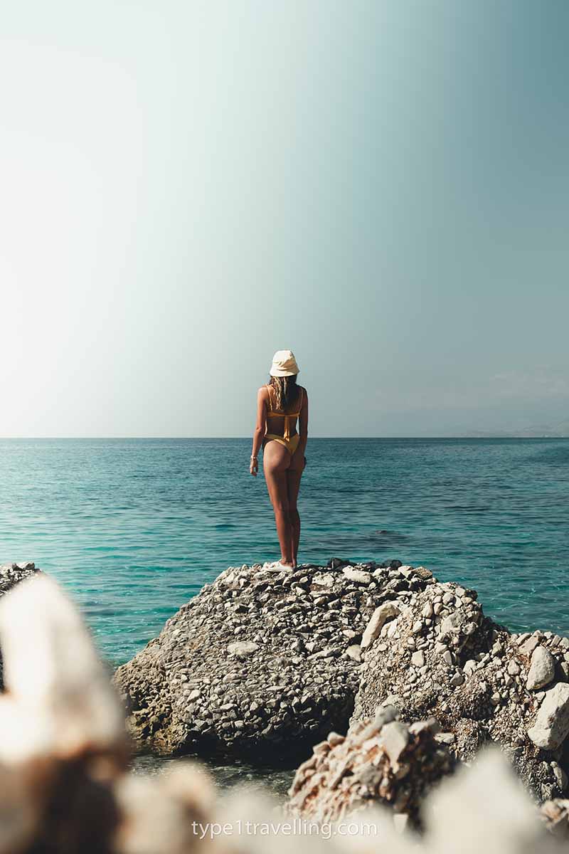 A woman standing on raised rocks close to the water of Kroreza Beach.