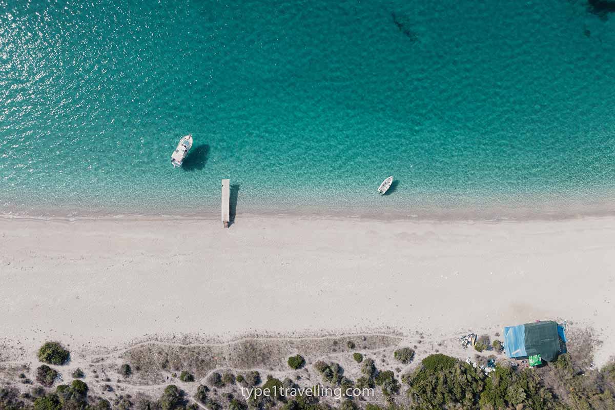 A small jetty and two boats close to the deserted shore of Kroreza Beach.