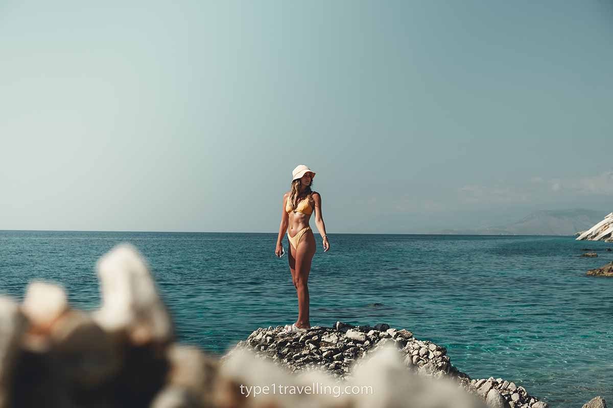 A woman standing on raised rocks close to the water of Kroreza Beach.