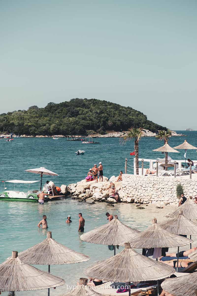 A handful of people in the water of a small beach which is lined with sun loungers straw umbrellas.