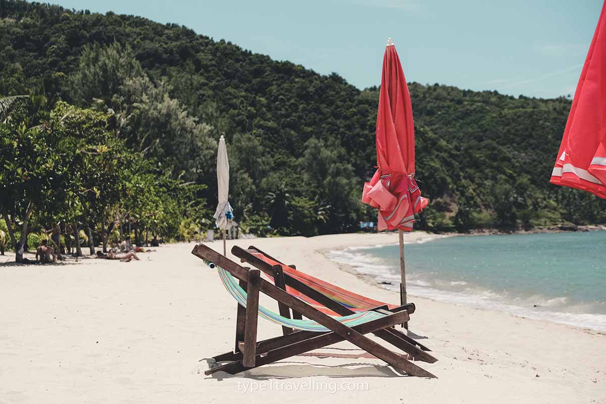 Two empty deck chairs and a couple of closed umbrellas on the white sand of Mae Haad Beach.