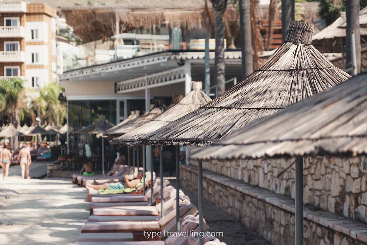 A line of sun loungers and straw parasols on a paved section next to Mucobega Beach.