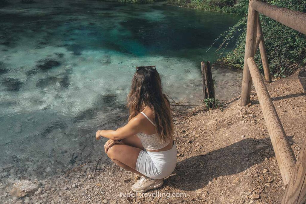 observing-syri-i-kalter A woman crouched next to the clear water of the Blue Eye natural spring.