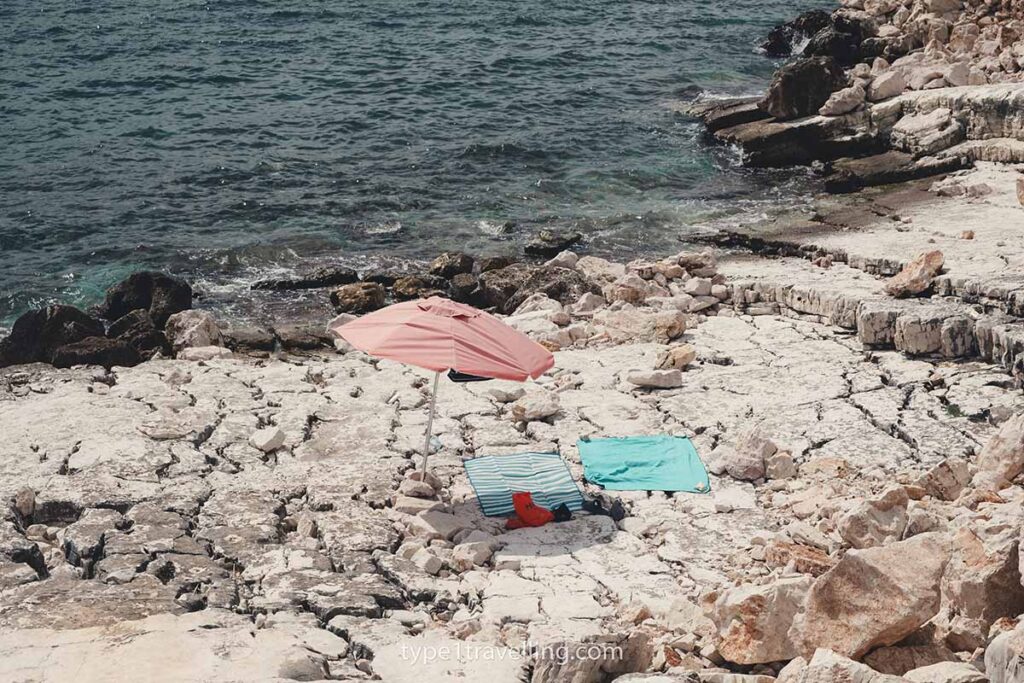 A single parasol and two beach towels lying on flat rocks.
