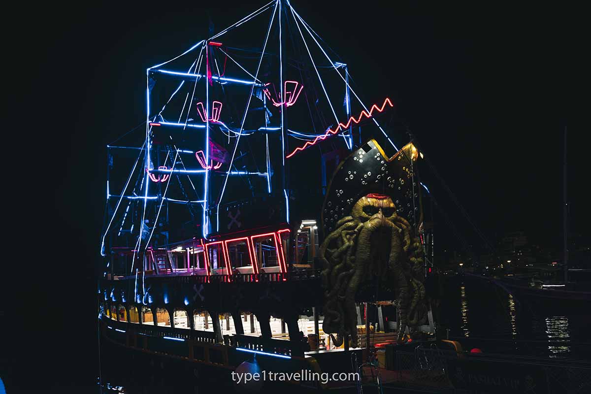 saranda-party-boat A sailboat which is lit up at night with strip lights.