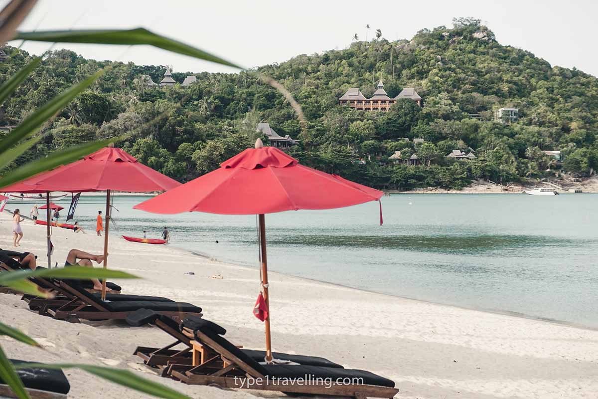 thong-nai-pan-noi A line of sun loungers and umbrellas on Thong Nai Pan Noi Beach with the headland and bungalows in the background.