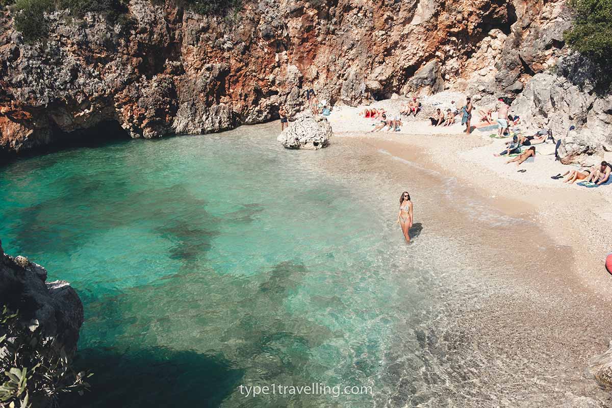 A woman standing ankle deep in the water of Aquarium Beach while other sunbathers lie on the beach.