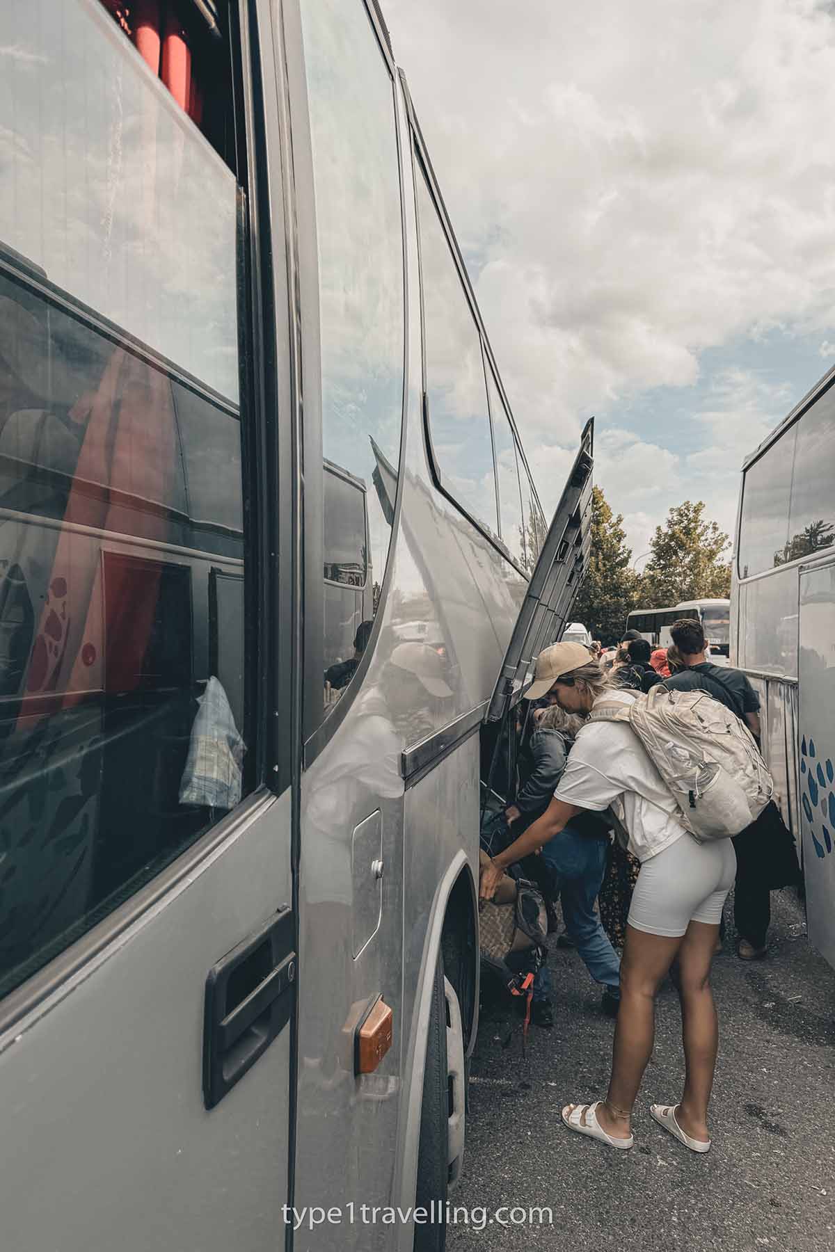 Passengers unloading their luggage from the underneath compartment of a large coach.