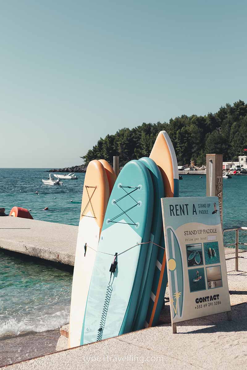 Several paddle boards stacked in two lines next to Himare jetty with as sign advertising them for rent.