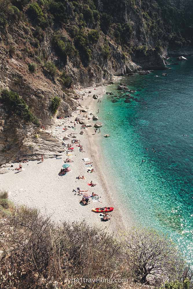 People sunbathing along the shoreline of Filikuri Beach which is backed by a steep rock face.
