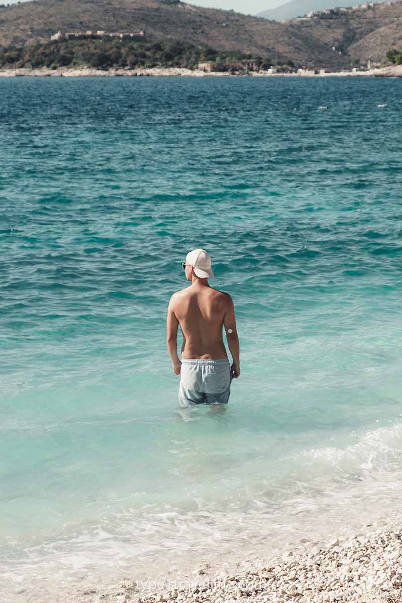 A man standing thigh-deep in the water of Porto Palermo Beach while looking out to sea.