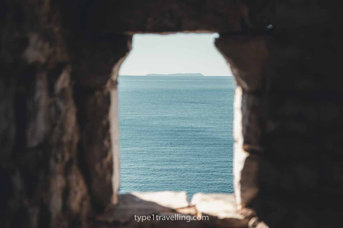 A distant island and the Ionian Sea seen through a stone window frame.