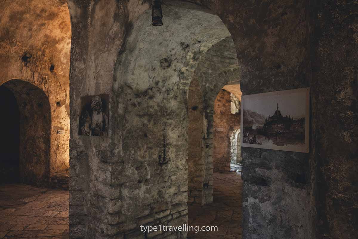 A couple of paintings hanging on the stone wall of a fortress interior with doorways breaking off in different directions.