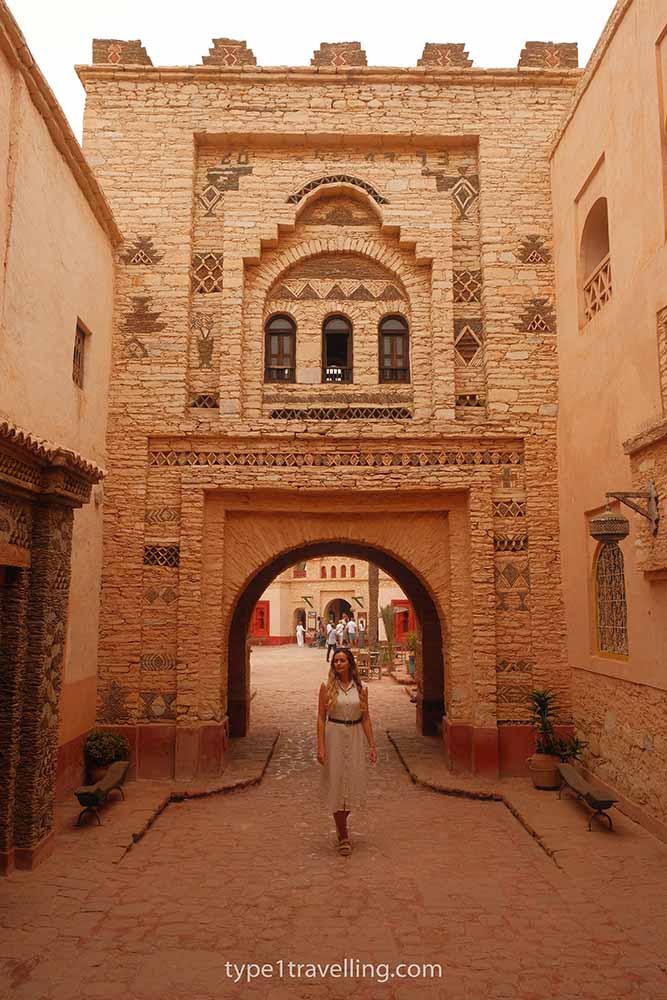 A woman posing in front of an ornate and intricately designed stone wall and archway.