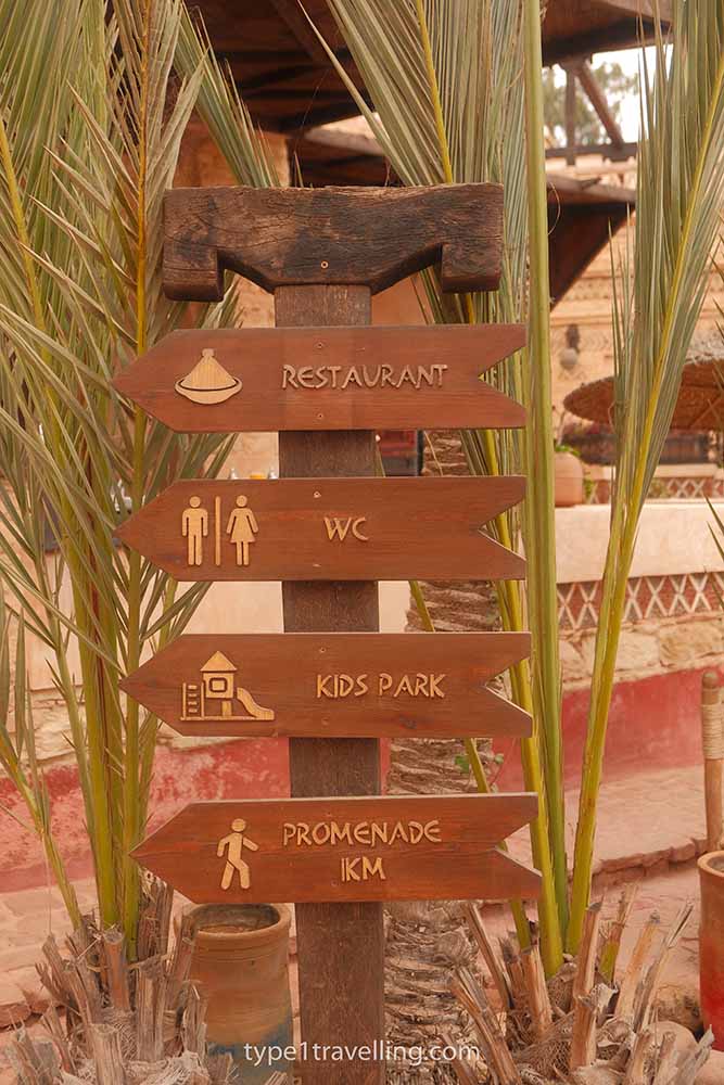 A wooden signpost for Restaurant, WC, Kids Park, and Promenade.