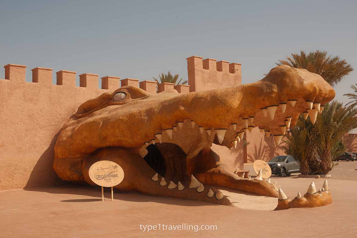 crocoparc-entrance A giant crocodile head statue in front of a red-coloured wall next to a sign for Crocoparc Agadir.