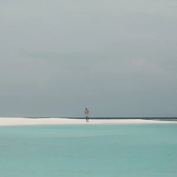 maldives A person standing on a strip of white beach surrounded by turquoise and deep blue water.