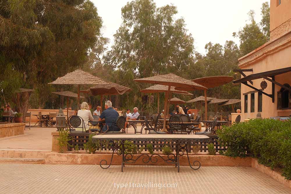 People sitting at several outdoor restaurant tables with umbrellas for shade.