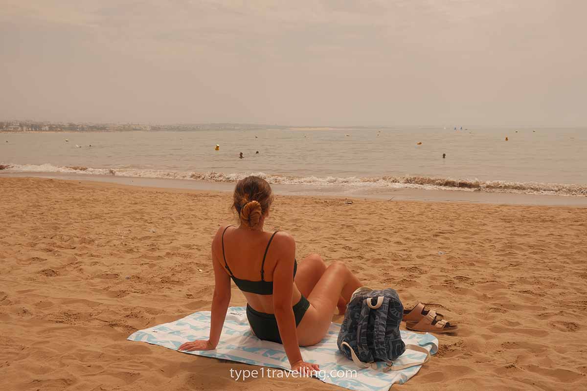 A woman sitting on a beach towel close to the water on Agadir Beach.